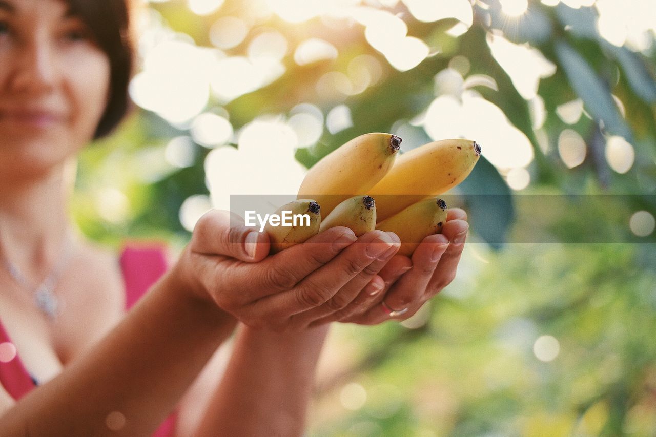 Woman holding bananas while standing outdoors