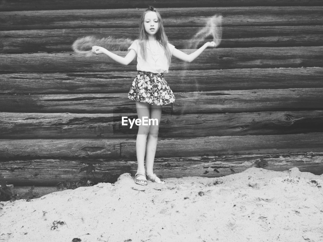 Girl playing with sand against wooden wall