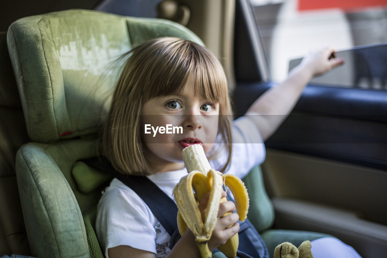 Portrait of cute girl eating banana while sitting in car