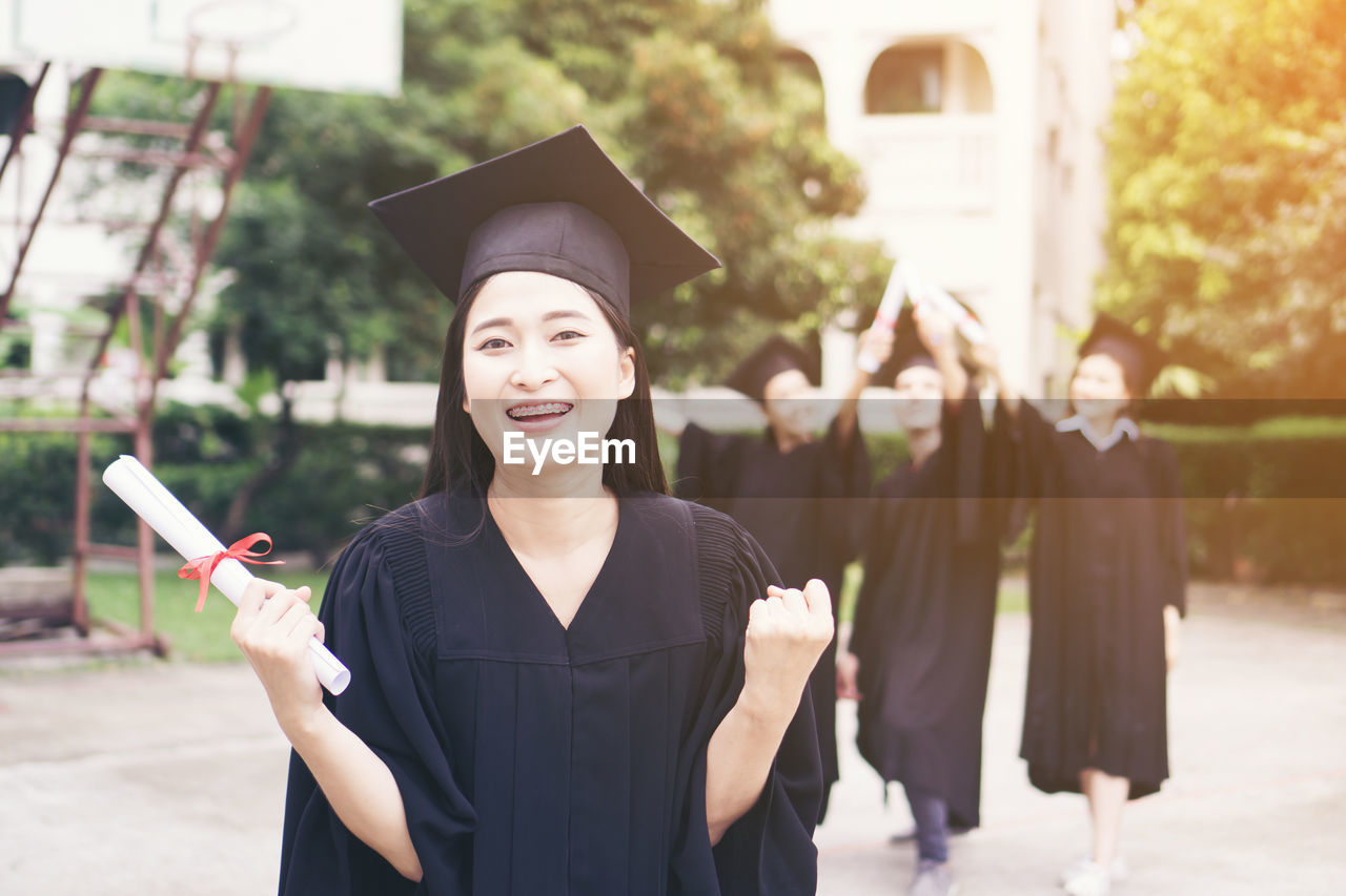 Cheerful student with clenched fist wearing graduation gown