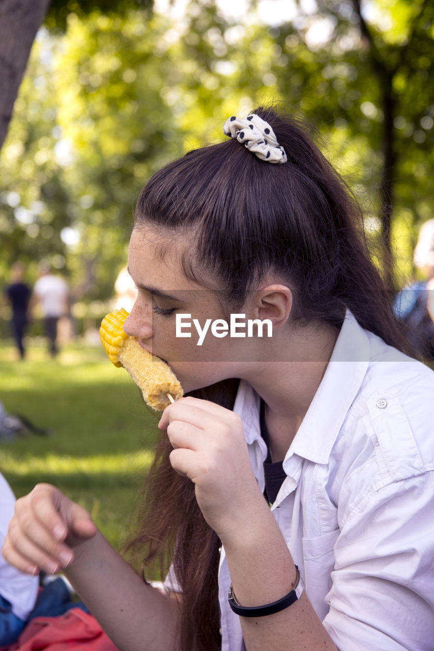 Close-up of young woman eating corn while sitting at park