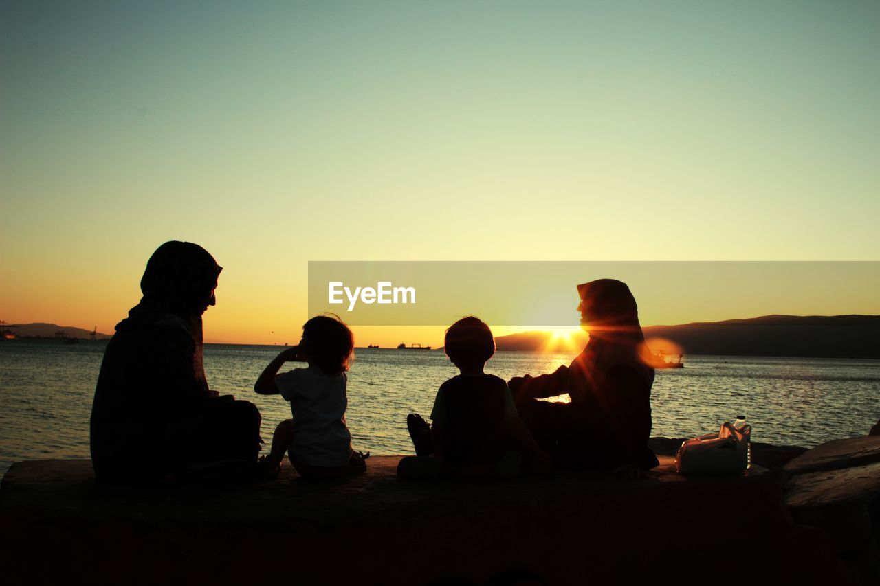 PEOPLE SITTING ON BEACH AT SUNSET