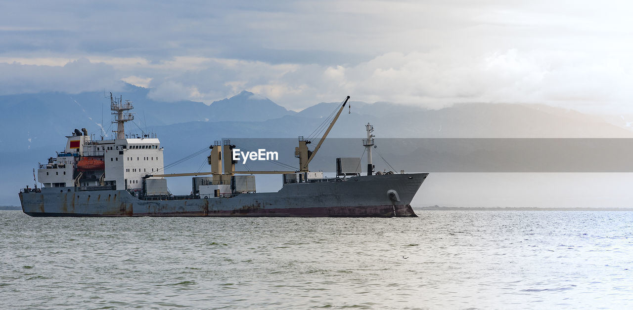 Large cargo container ship sailing against the volcano