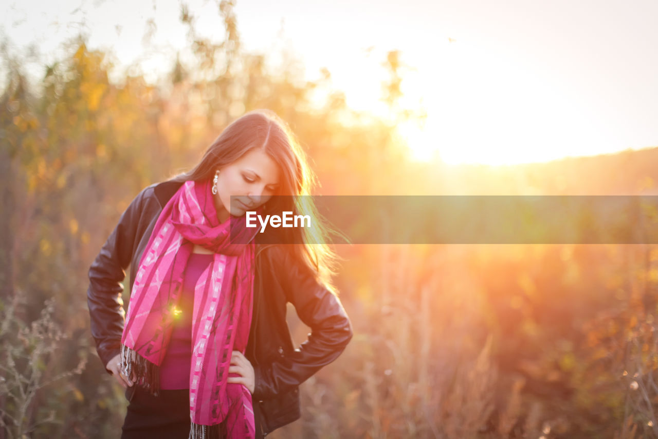BEAUTIFUL WOMAN STANDING ON FIELD AGAINST SKY AT SUNSET
