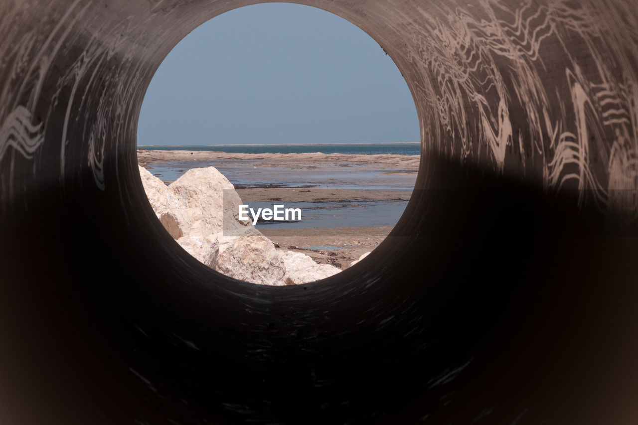 Beach against clear sky seen through pipe