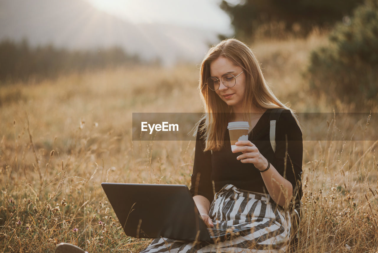 Happy woman freelancer with glasses working on laptop, remote location in nature