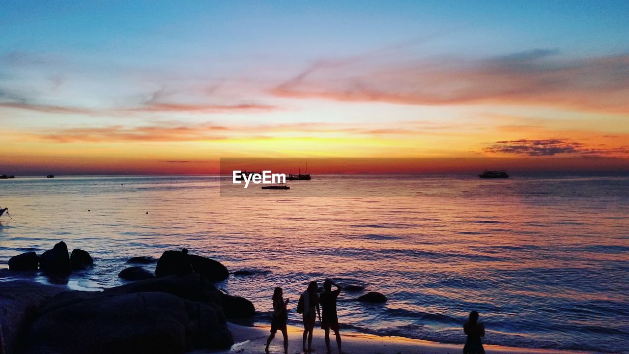 Silhouette people at beach against sky during sunset