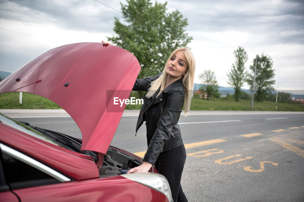 Young woman with broken car on road