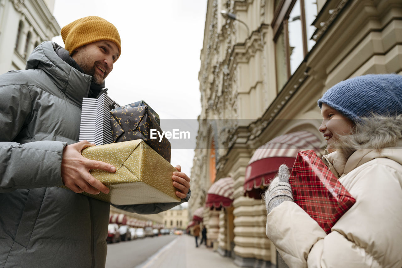 Smiling father and daughter holding christmas gifts at city street