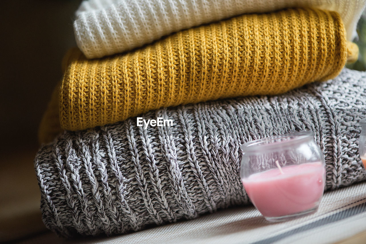 Close-up of tea light candle by stacked sweaters on table