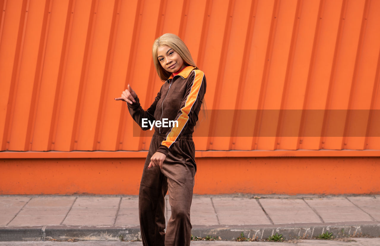 Cheerful african american woman in sportswear dancing in the street on an orange background