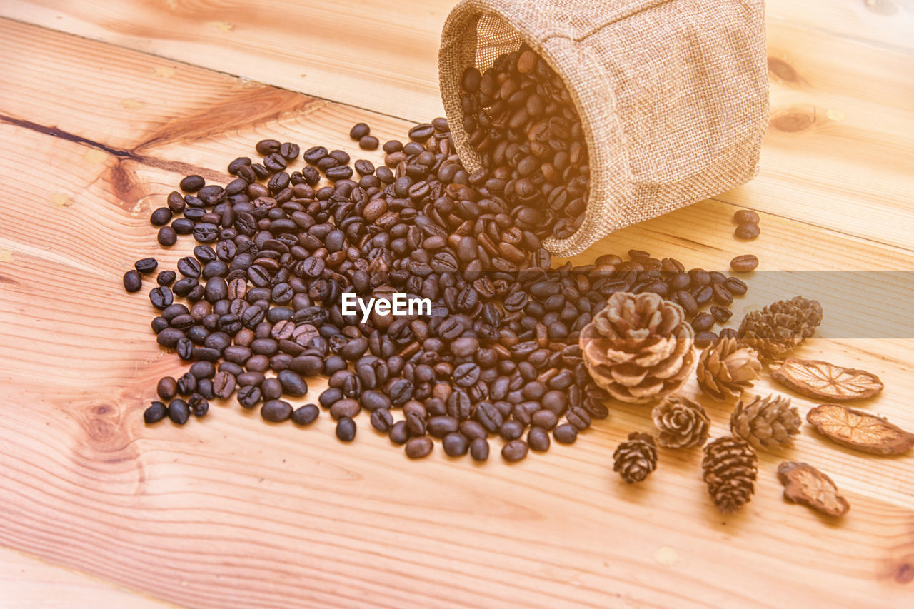 High angle view of roasted coffee beans with pine cones on wooden table