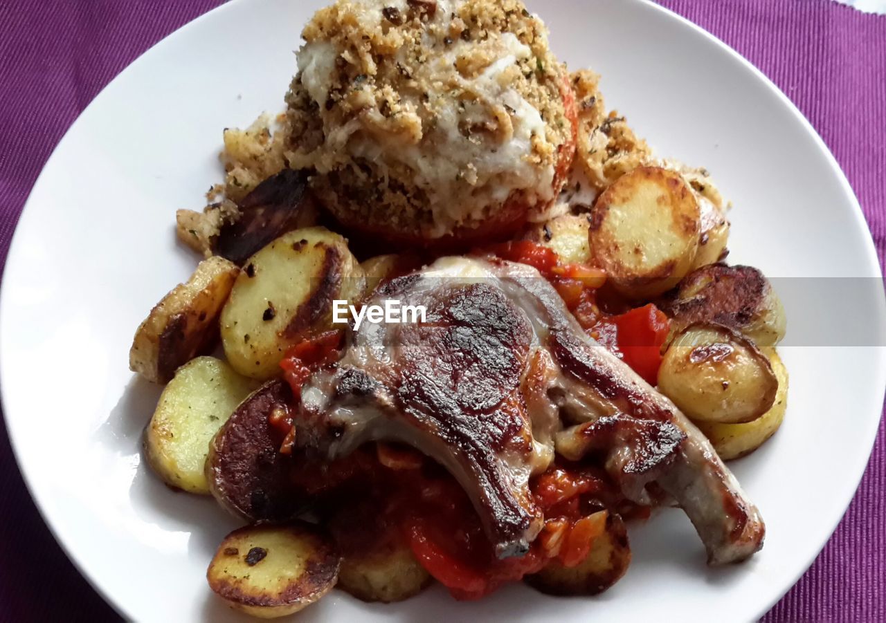 Close-up of lamb meat with fried potatoes and tomato served on table