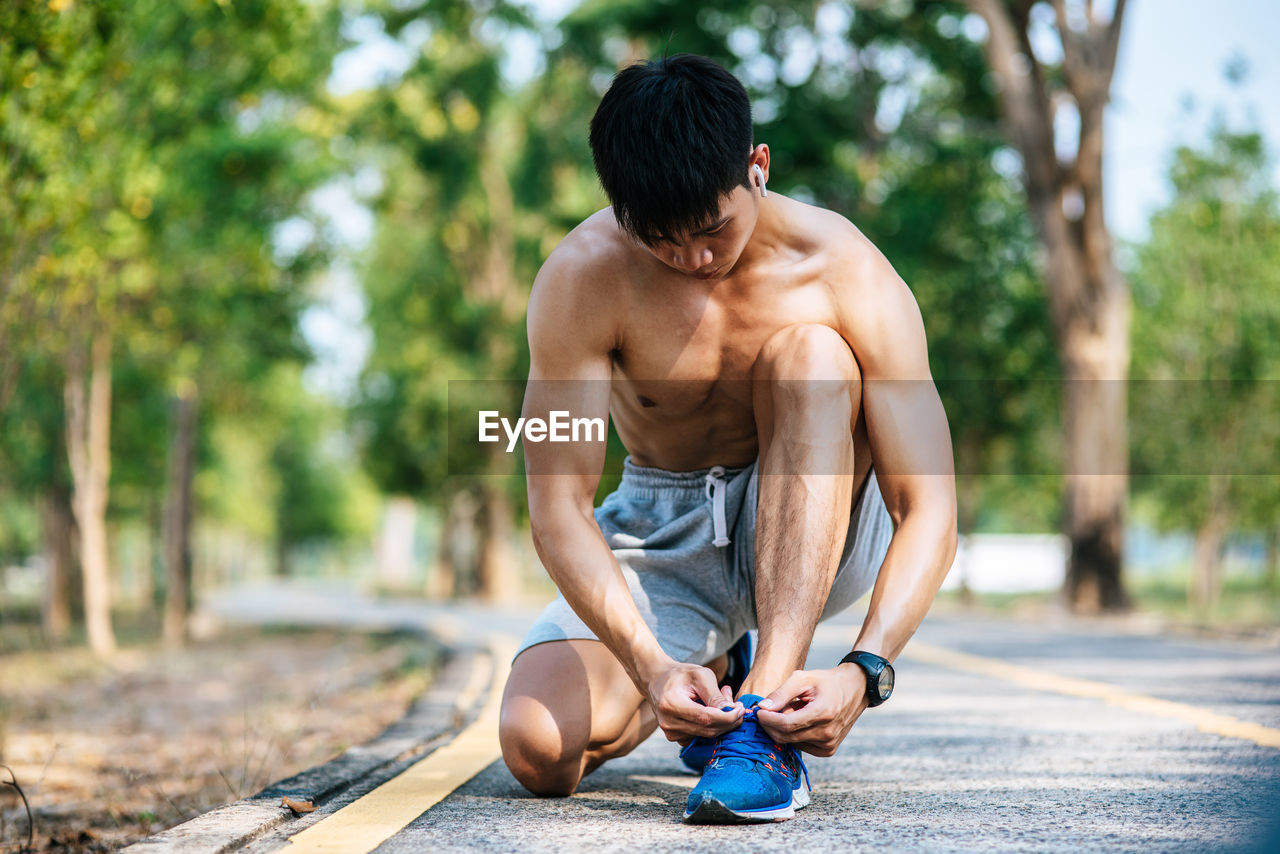 FULL LENGTH OF SHIRTLESS MAN SITTING ON PLANT