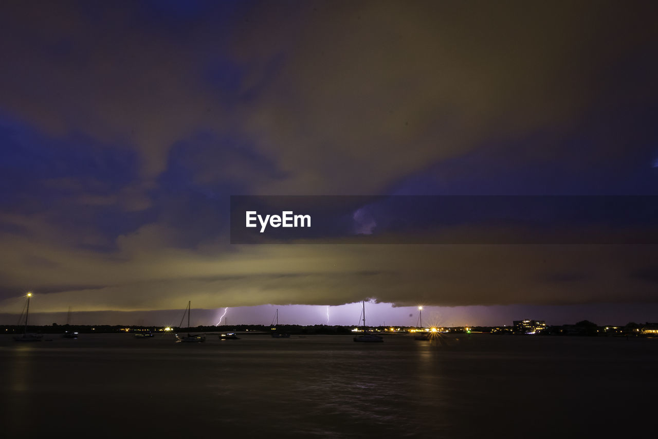 ILLUMINATED COMMERCIAL DOCK AGAINST SKY AT NIGHT