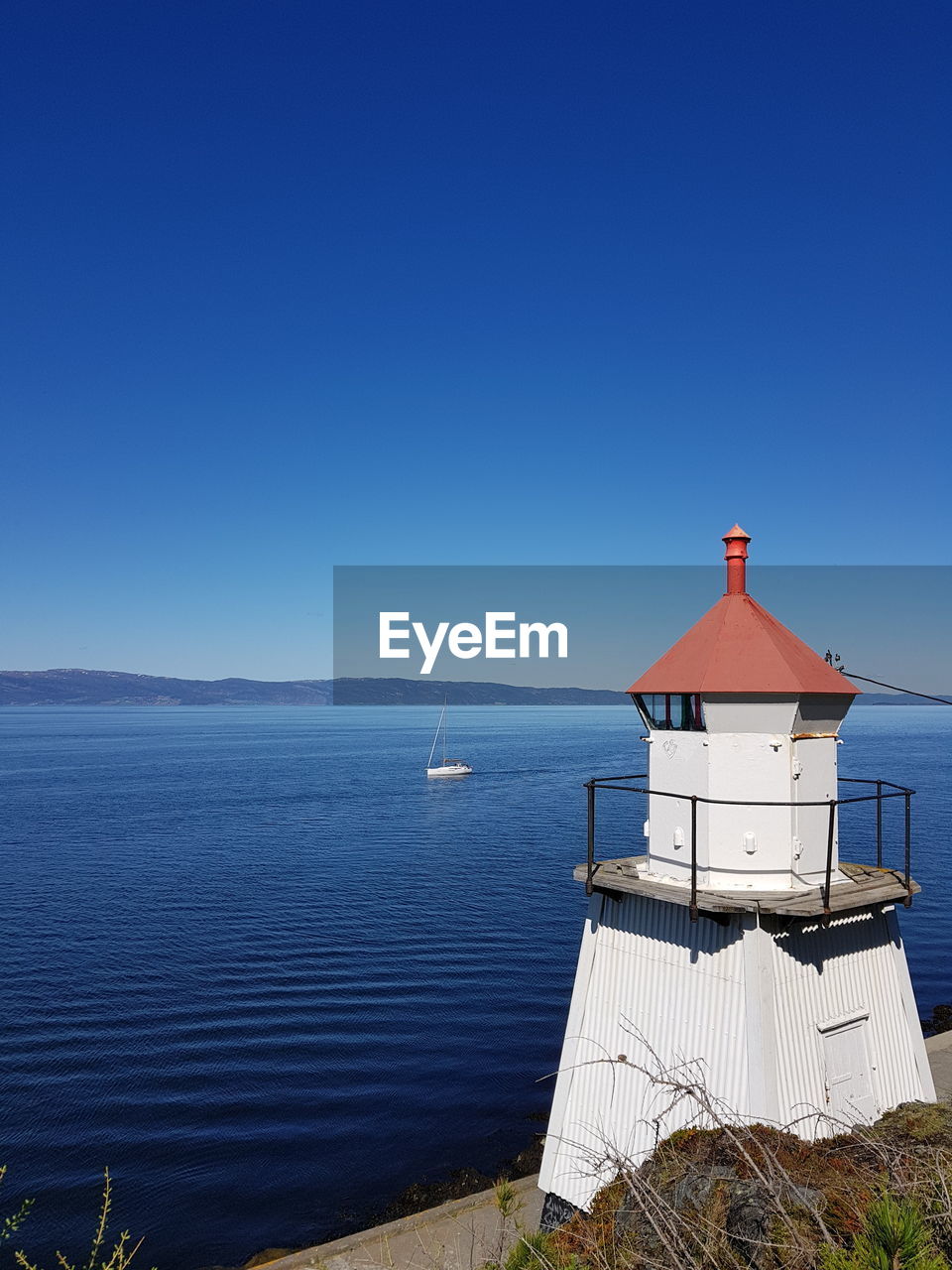 Lighthouse by sea against blue sky