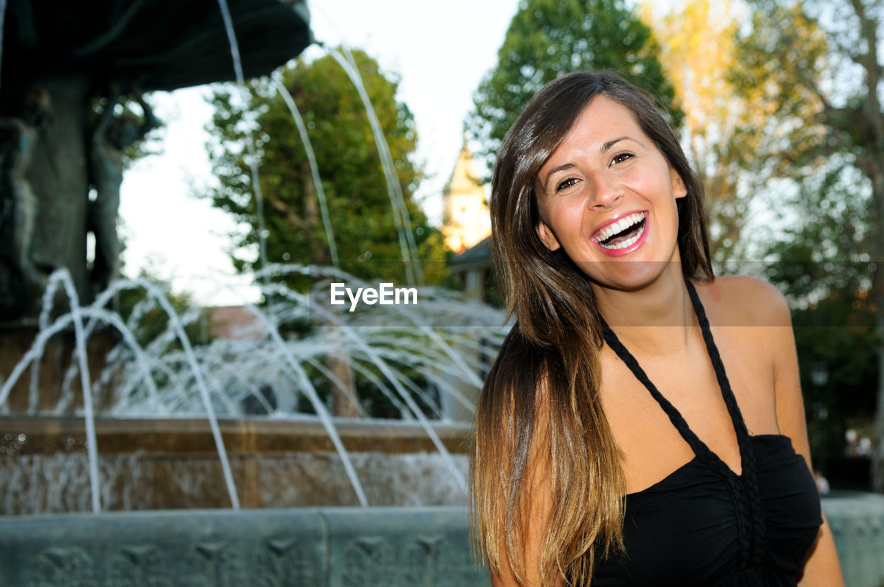 Portrait of happy young woman standing against fountain