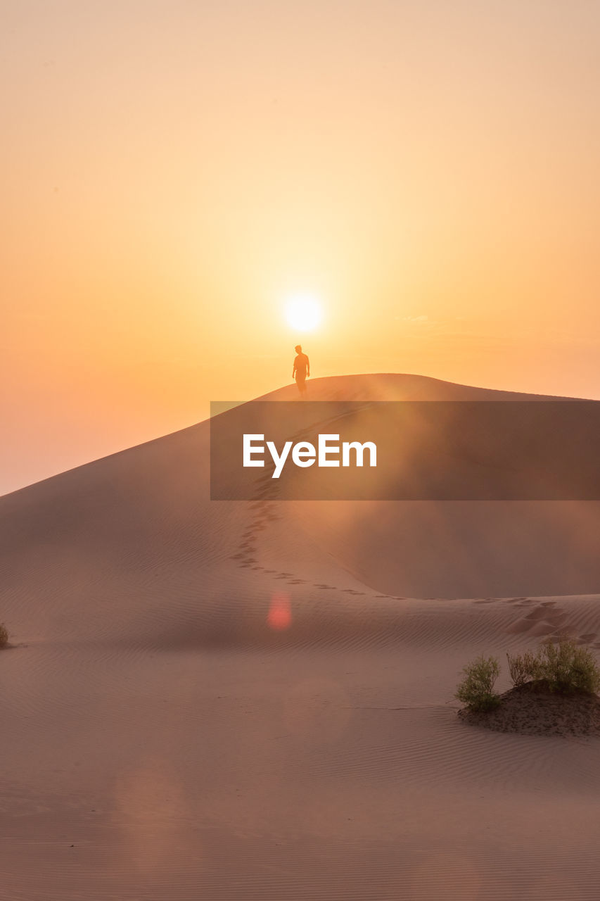 Solo traveler walking down dune against sunrise.