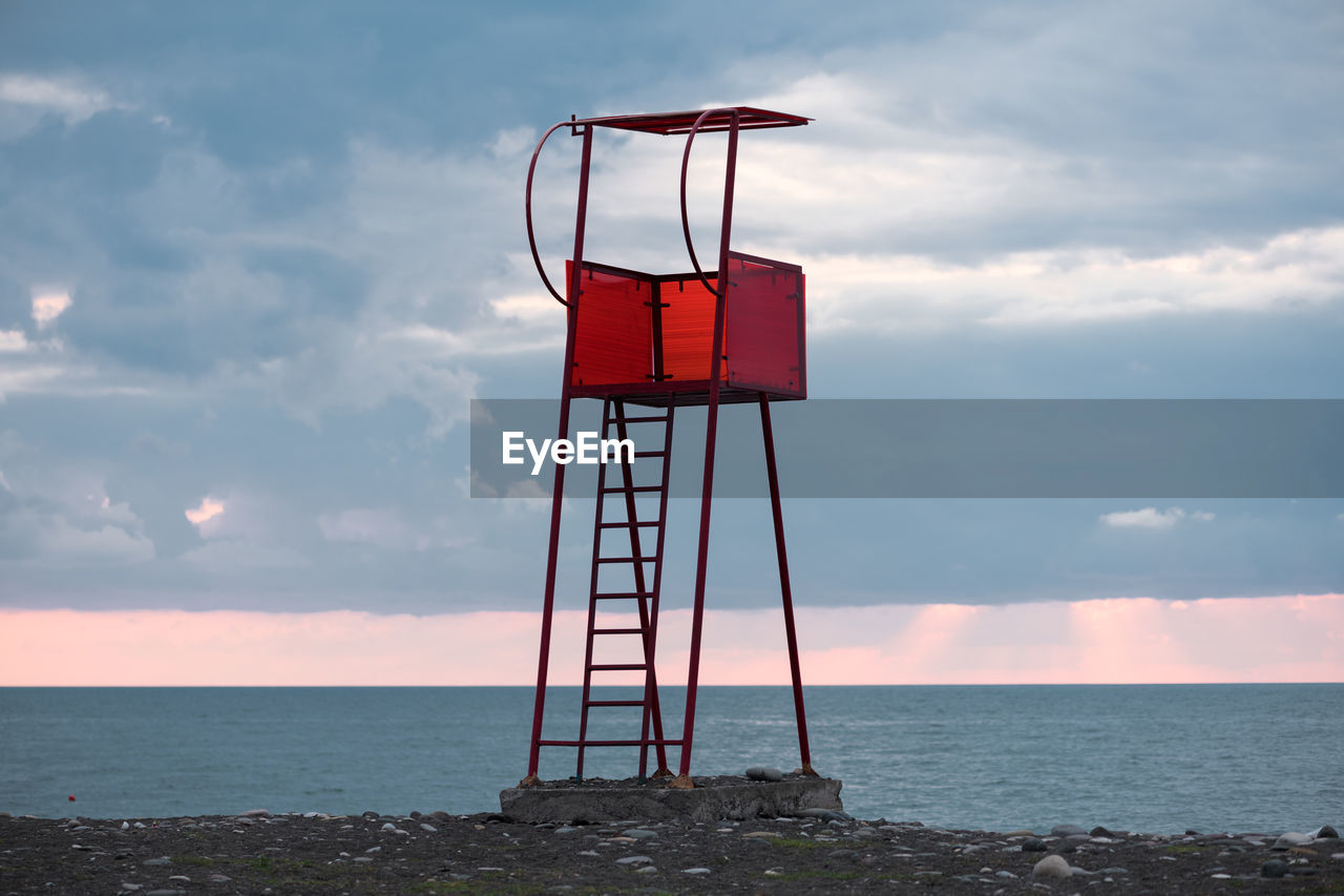 A red lifeguard post stands vibrantly against a black sea seascape on an empty beach in batumi.