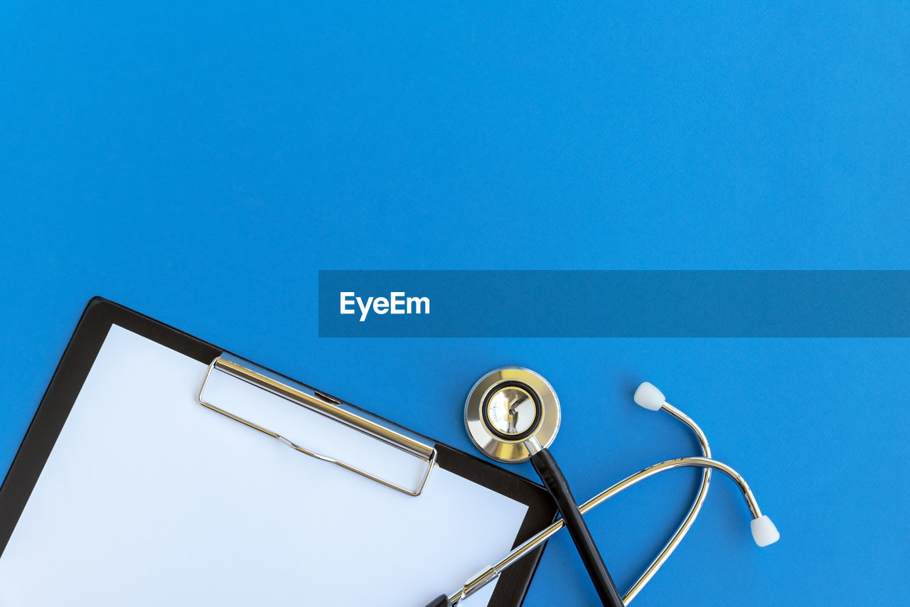 Directly above shot of stethoscope and clipboard against blue background