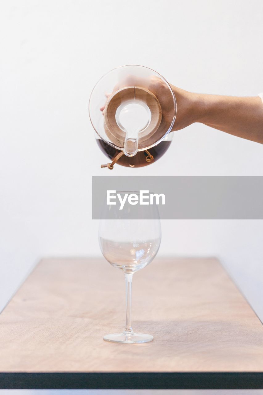 Cropped hand pouring drink in wineglass on table against white background