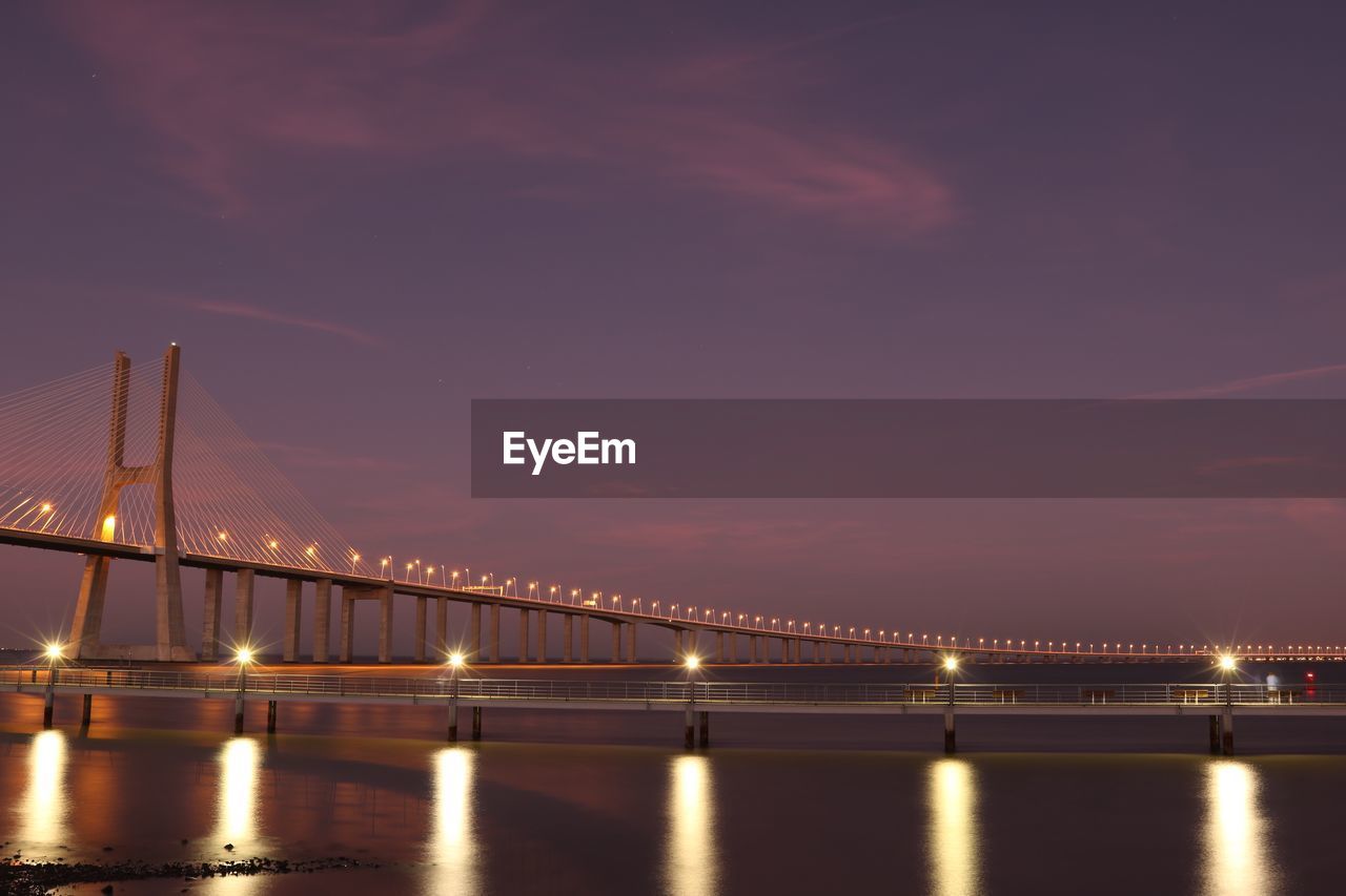 Illuminated bridge over river against sky at night