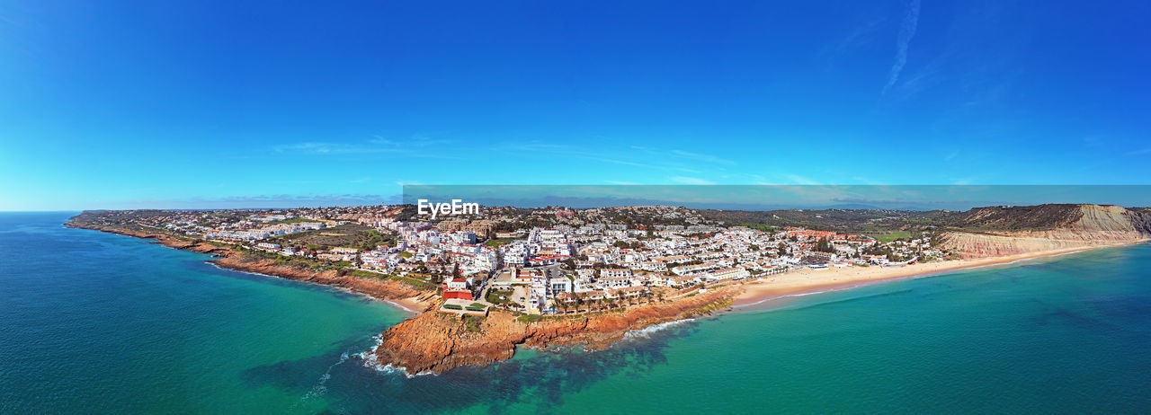 HIGH ANGLE VIEW OF SEA AMIDST BUILDINGS AGAINST BLUE SKY