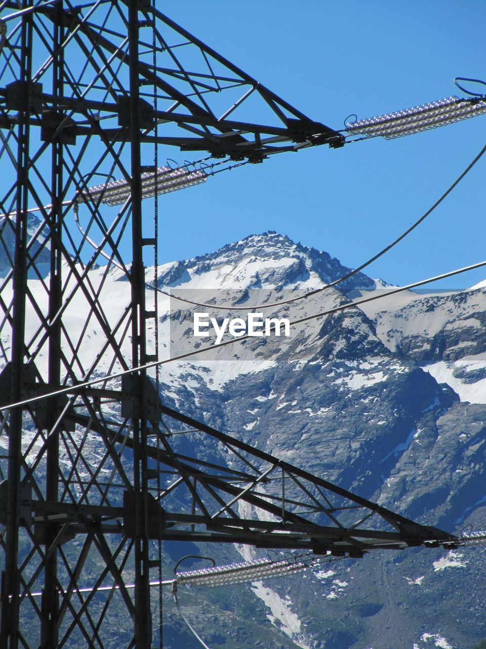 Cropped electricity pylon against snow covered mountain and blue sky