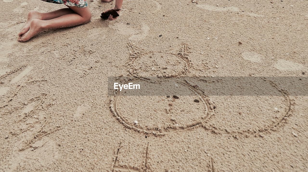 Low section of girl kneeling beside drawing in sand