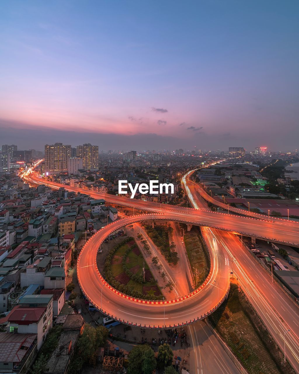 Aerial view of light trails on road amidst buildings against sky during sunset