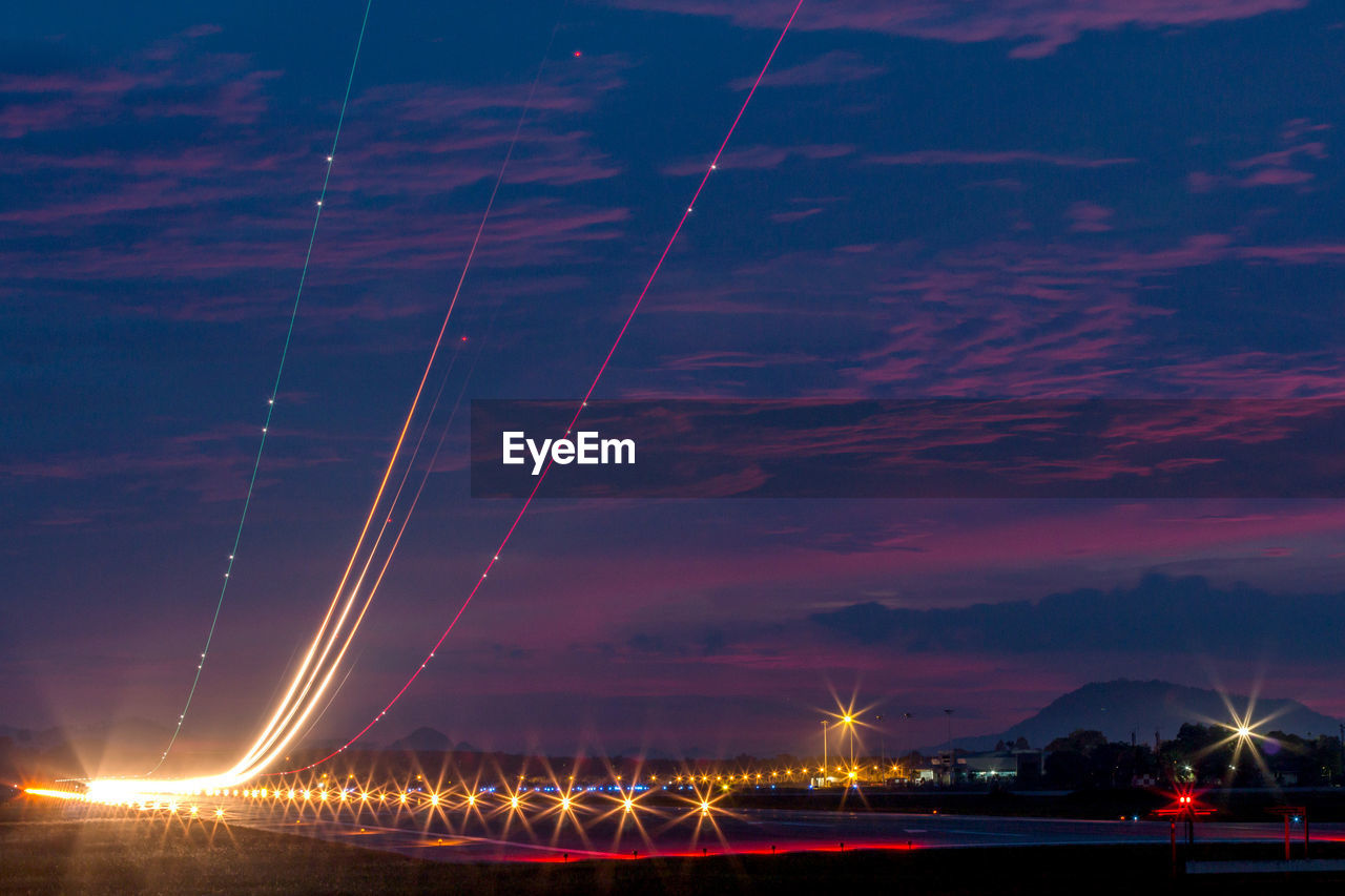 Light trails at airport runway against cloudy blue sky at dusk