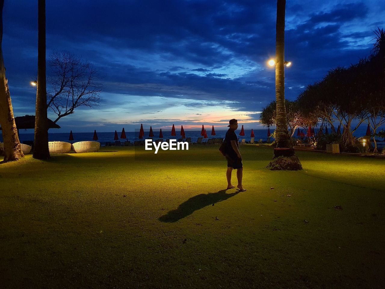 MAN WALKING ON ILLUMINATED STREET AGAINST SKY