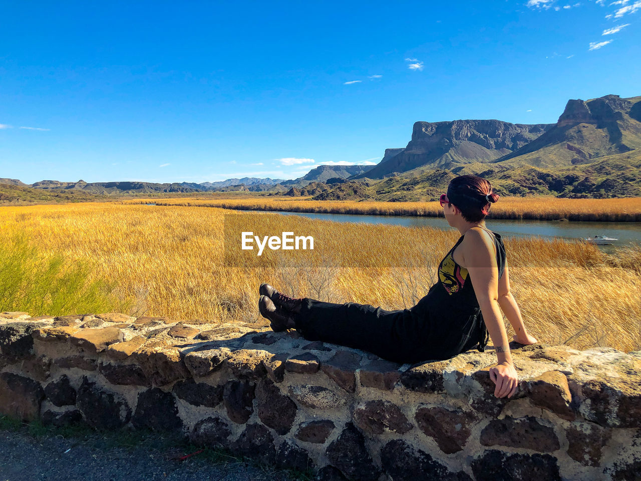 Side view of woman sitting on landscape against sky