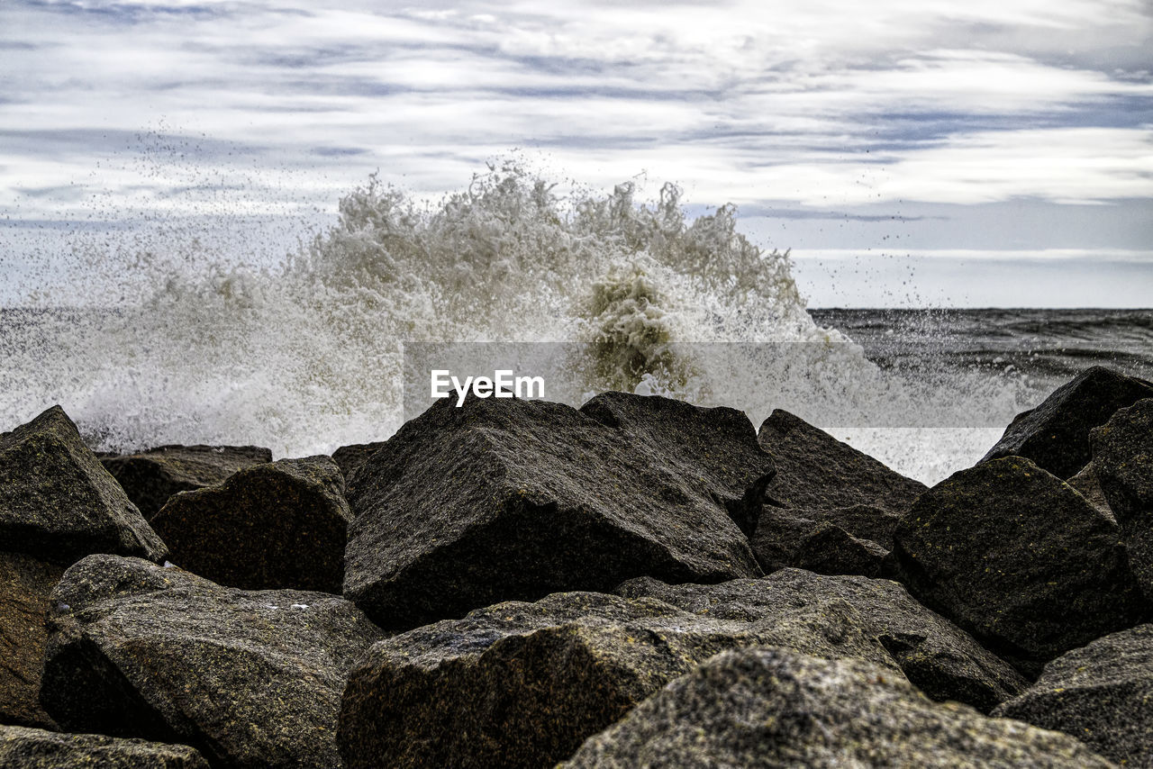 SEA WAVES SPLASHING ON ROCKS AGAINST SKY