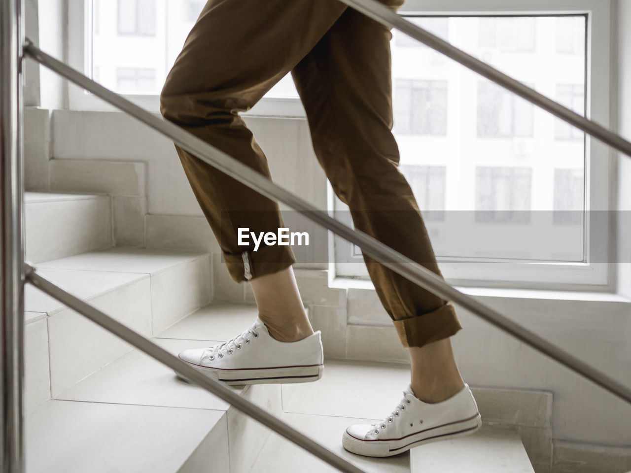Woman in white sneakers and khaki trousers goes upstairs. white staircase in apartment building. 