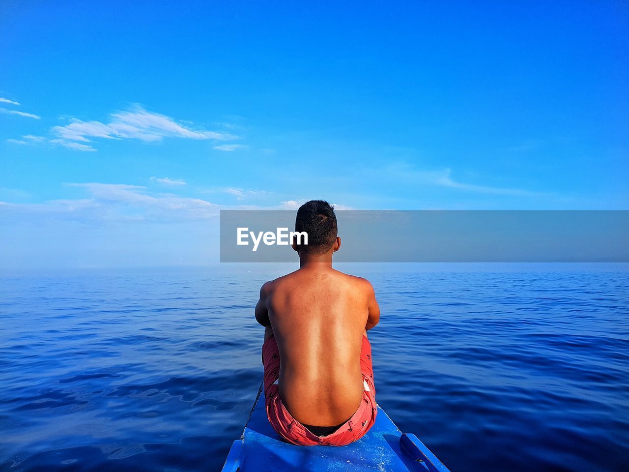 Rear view of shirtless man on boat in sea