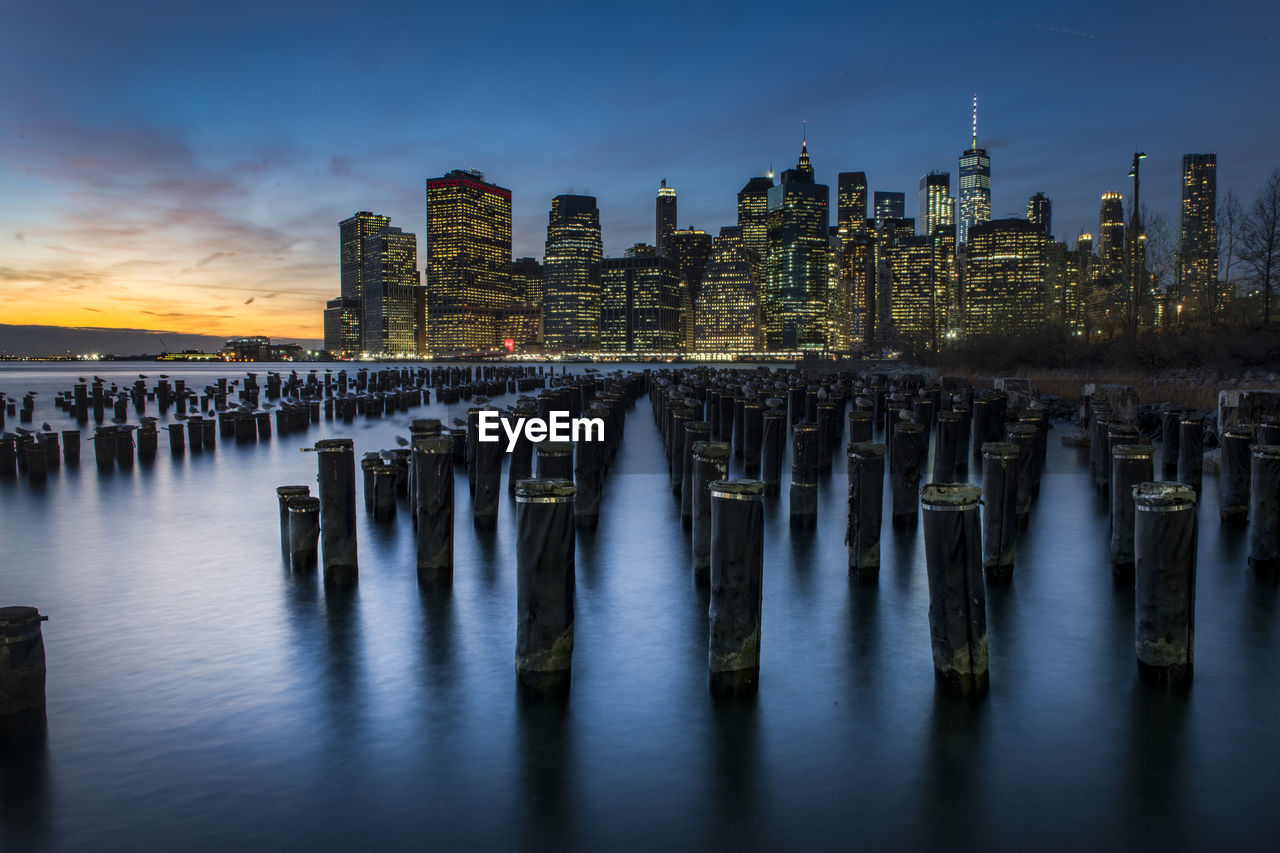 Wooden posts in sea against sky at dusk. skyline in background. manhattan at dusk.
