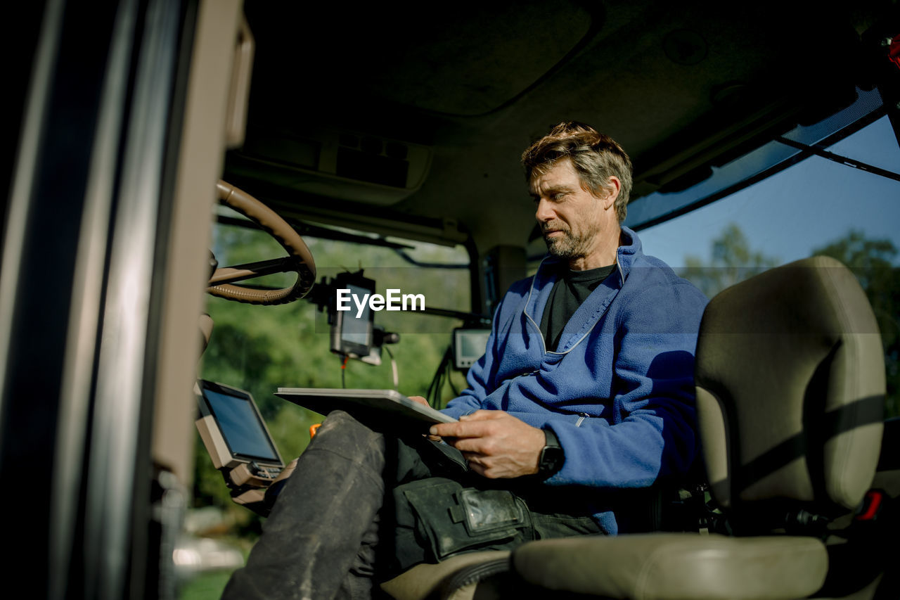 Mature farmer using tablet pc sitting in tractor on sunny day