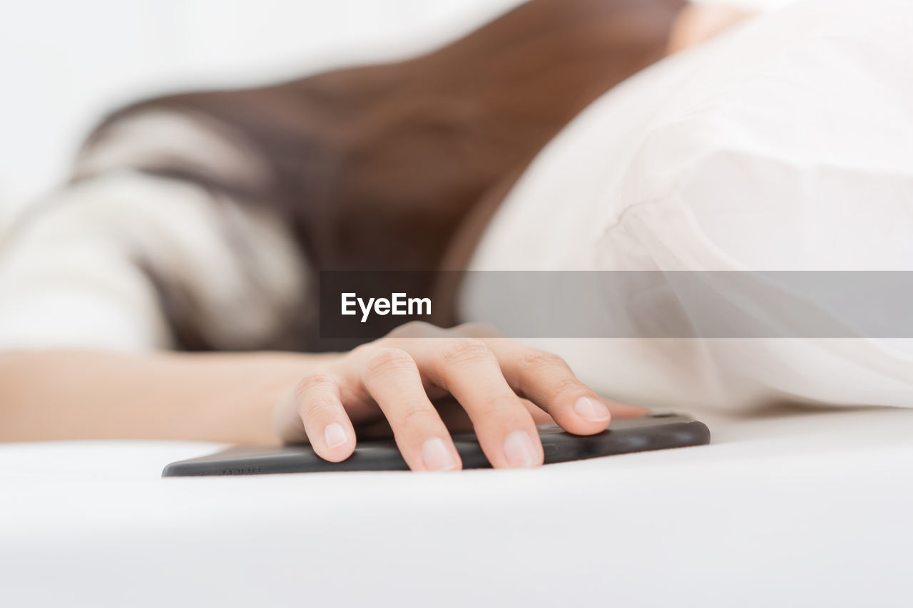 Close-up of woman hand holding mobile phone while lying on bed