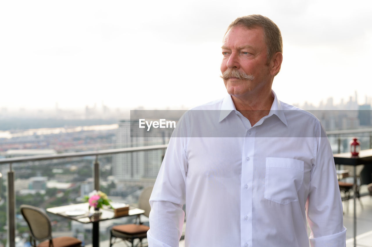 Senior man looking away against cityscape