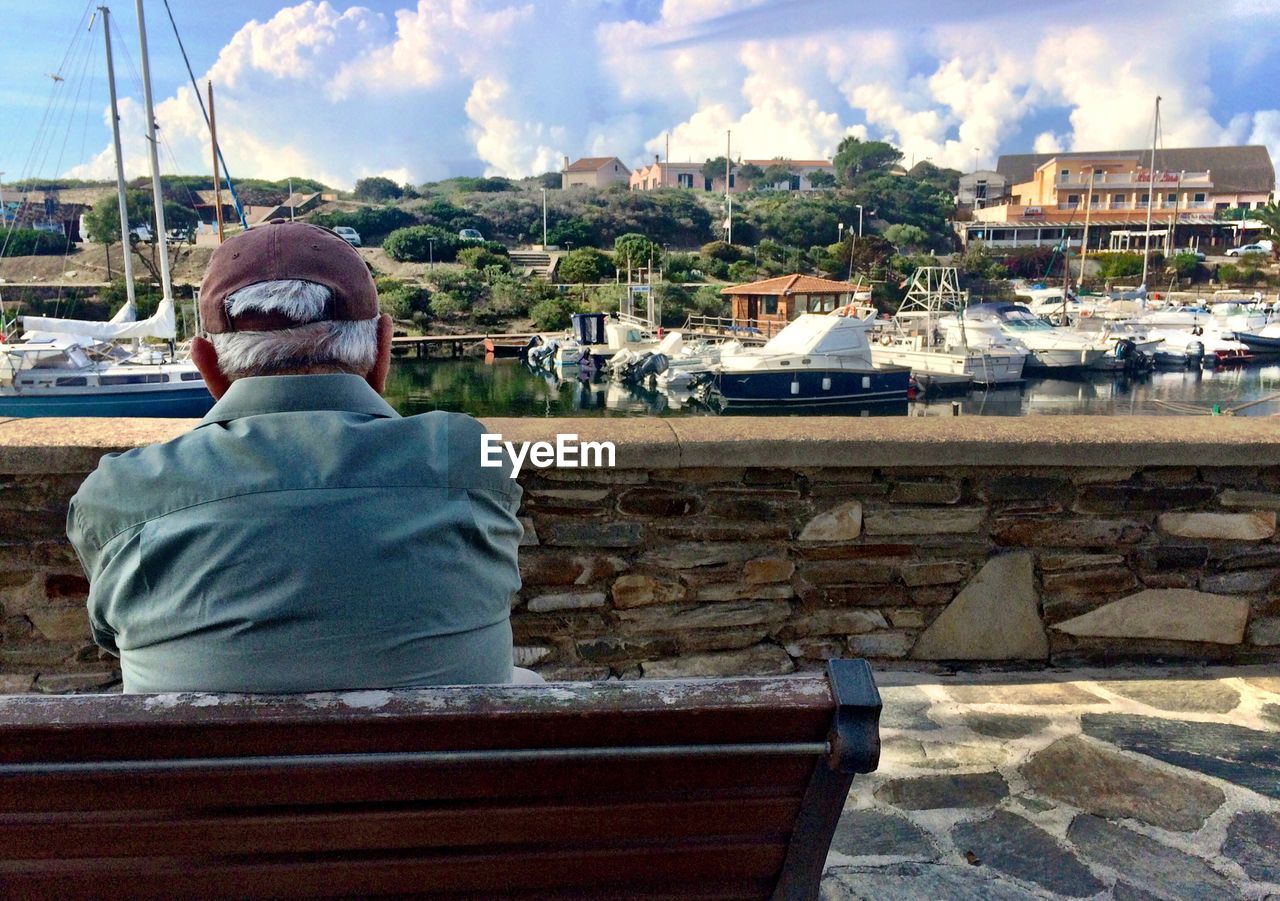 Rear view of senior man sitting on bench against harbor