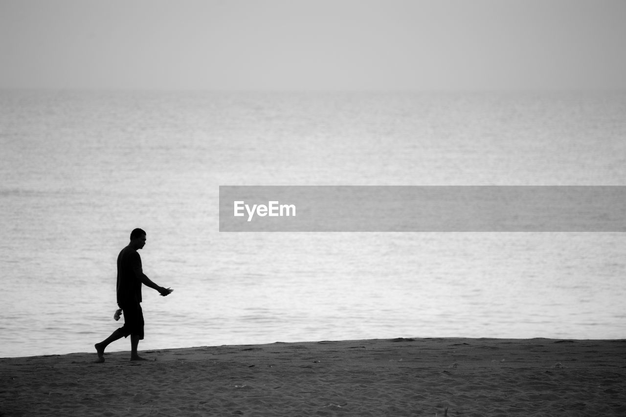 Silhouette man walking on beach against sky