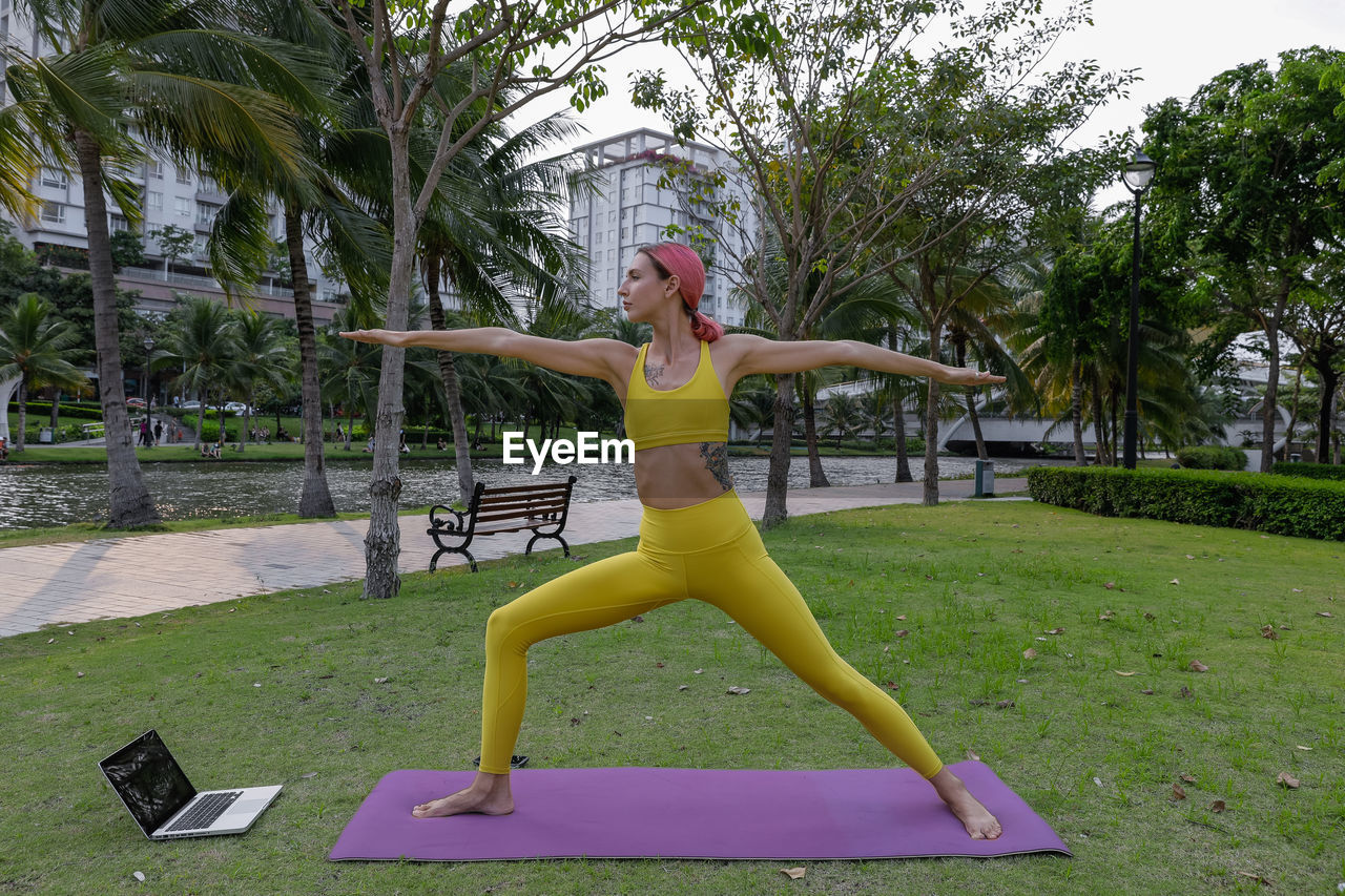 Woman with arms raised on grass against trees