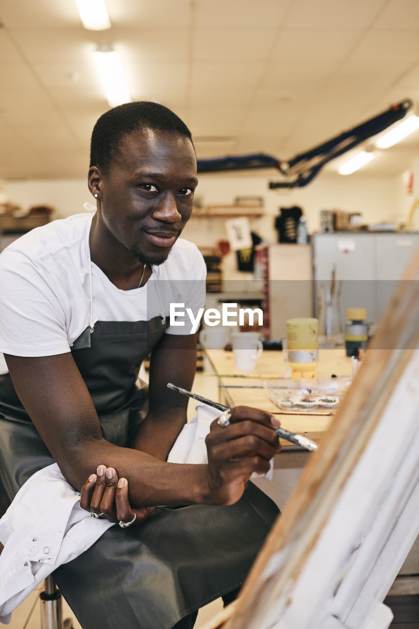 Portrait of young man painting while sitting in art class