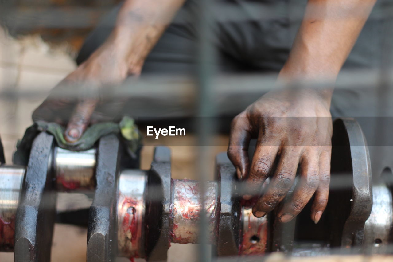 Midsection of greasy mechanic hands on machinery at workshop