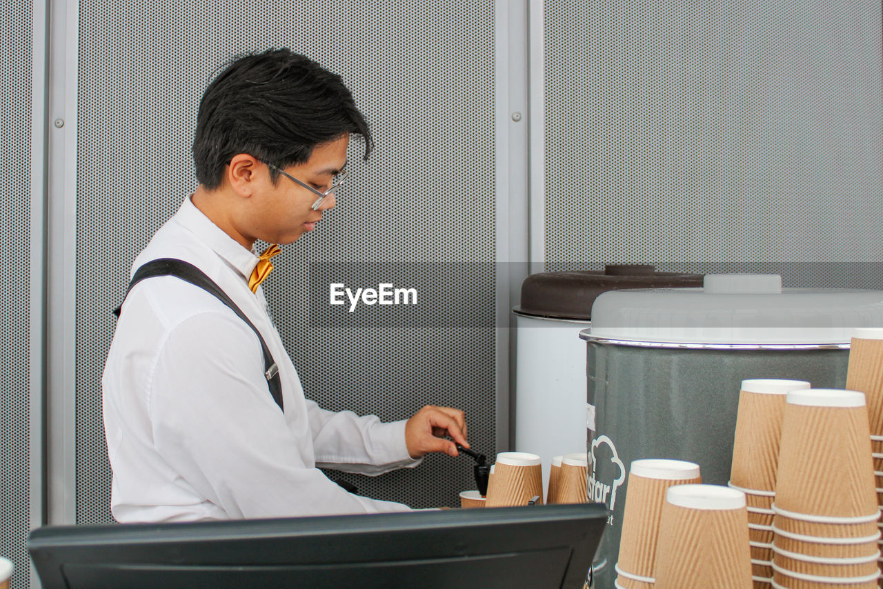 Side view of man taking coffee from machinery in office