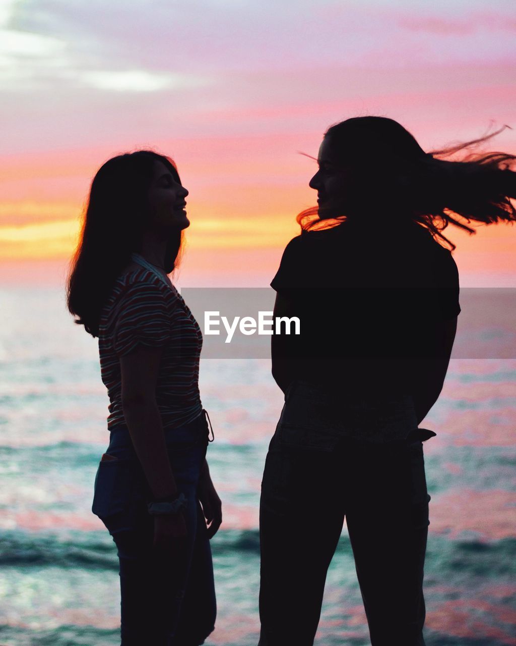 Friends standing against sea during sunset