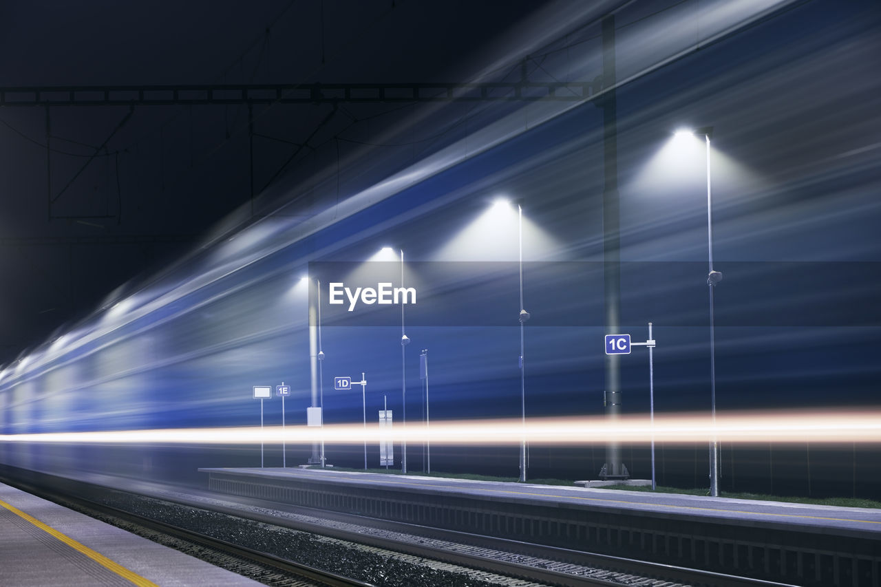 Railway at night. light trails of passenger train at illuminated railroad station.