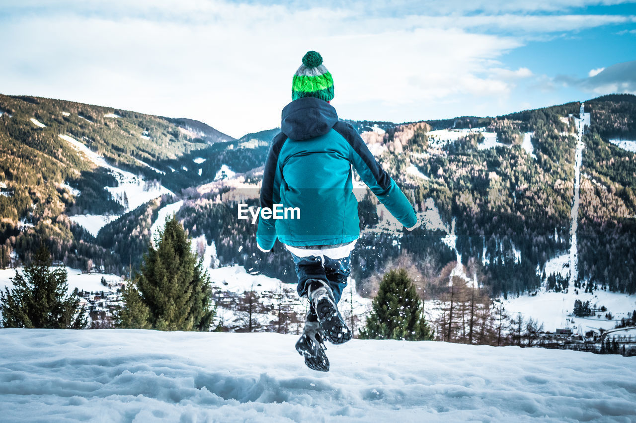 Rear view of boy jumping on snowfield against mountains