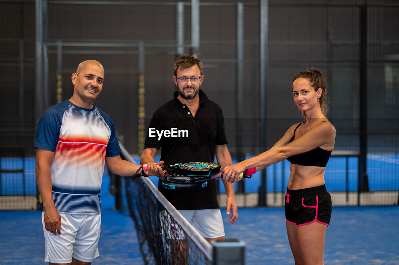 Portrait of smiling sportsman's posing indoor on padel court with rackets and balls